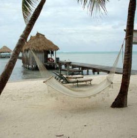 Belize hammock on the shoreline wiht palm trees and over the water hut – Best Places In The World To Retire – International Living